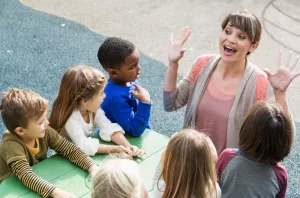 Story-Based Coaching with Adventures in Wisdom. Female Coach Hands Up Group of Kids